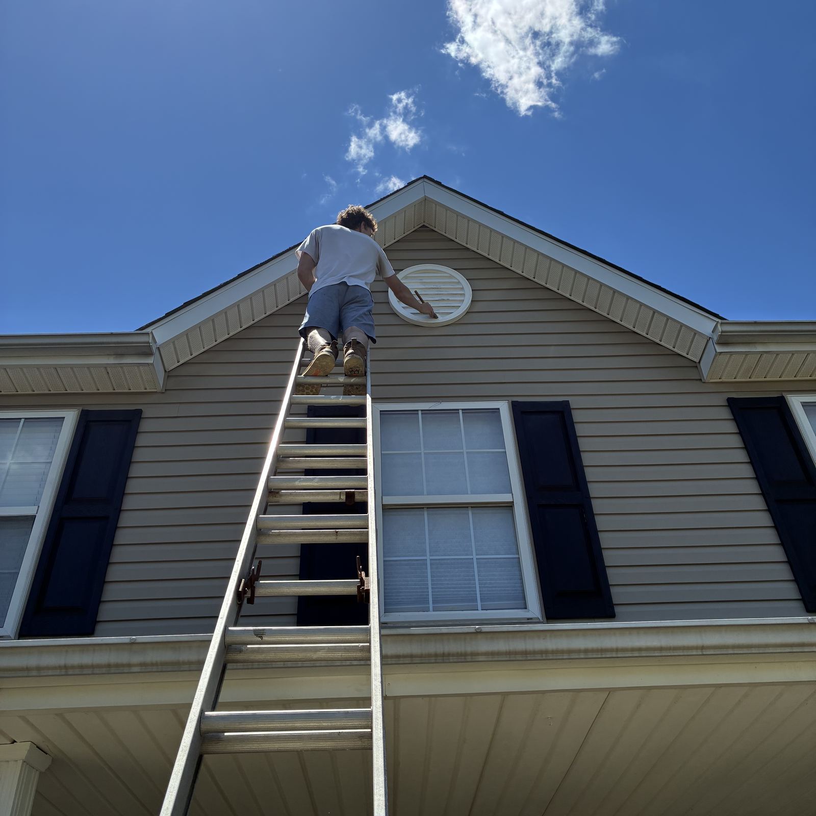Painter on a ladder carefully hand-brushing trim detail high on a home