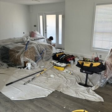 Living room furniture and floors fully covered with drop cloths and plastic before painting